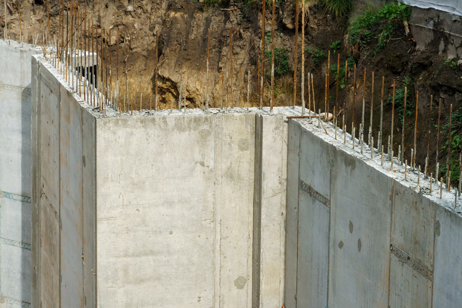 Muro de arrimo em concreto armado segurando um desnível de terra, com as barras de espera aparentes no topo